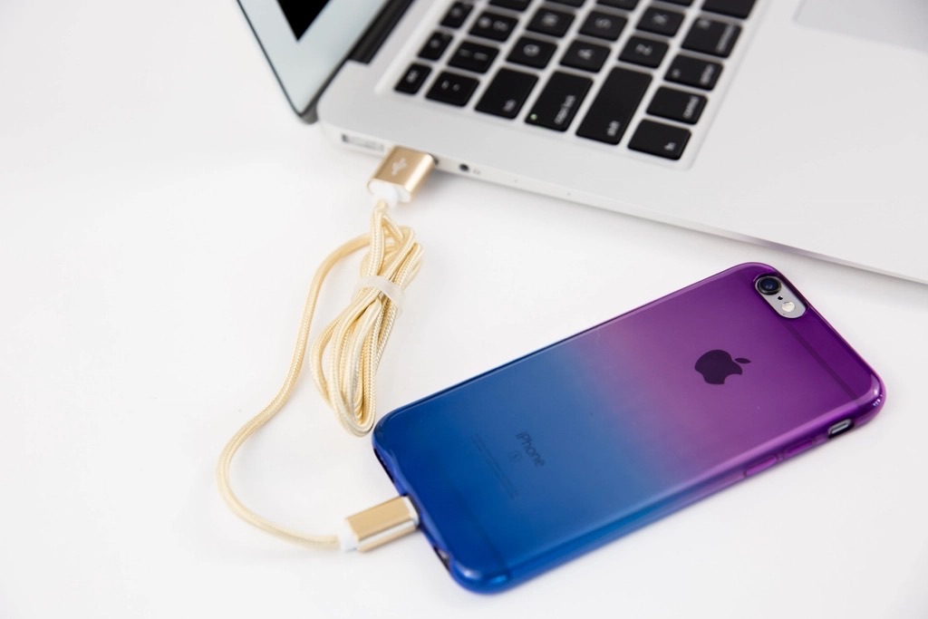 An iPhone connected by cable to a MacBook on a white desk