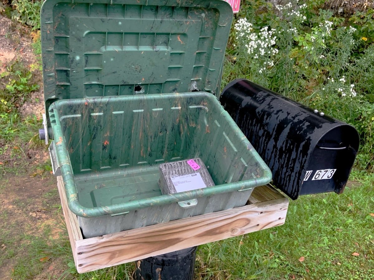 A parcel waiting in an open green delivery box next to a black roadside mailbox