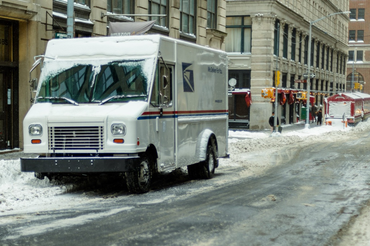 A white mail truck parked on a snowy city street in winter