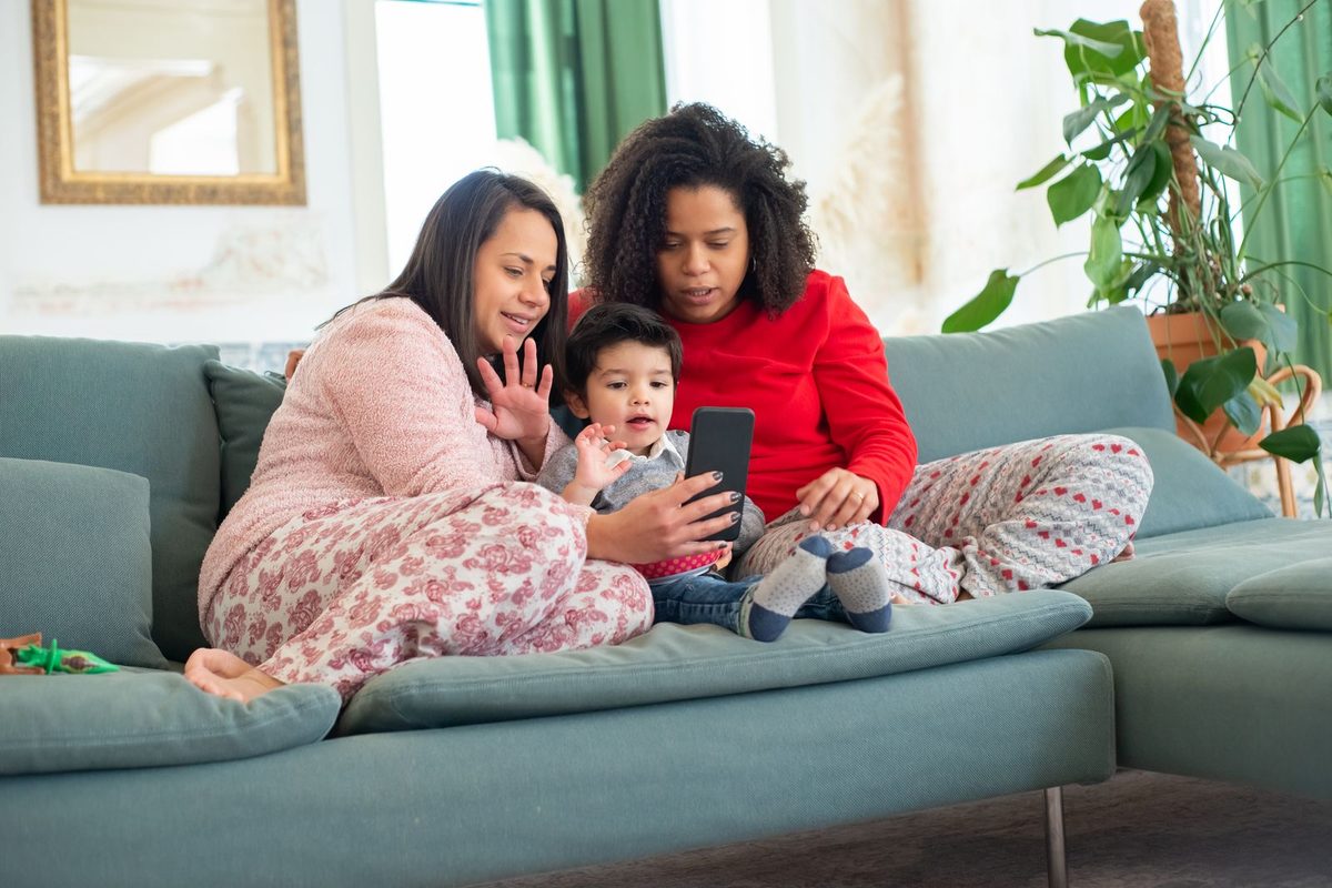Two women and a toddler on a green sofa, all looking at one smartphone