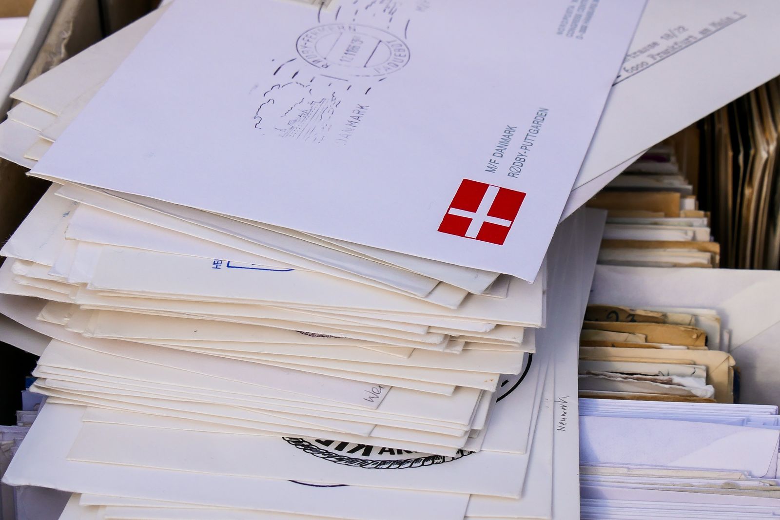A tall stack of white envelopes in a box, the top one stamped and addressed