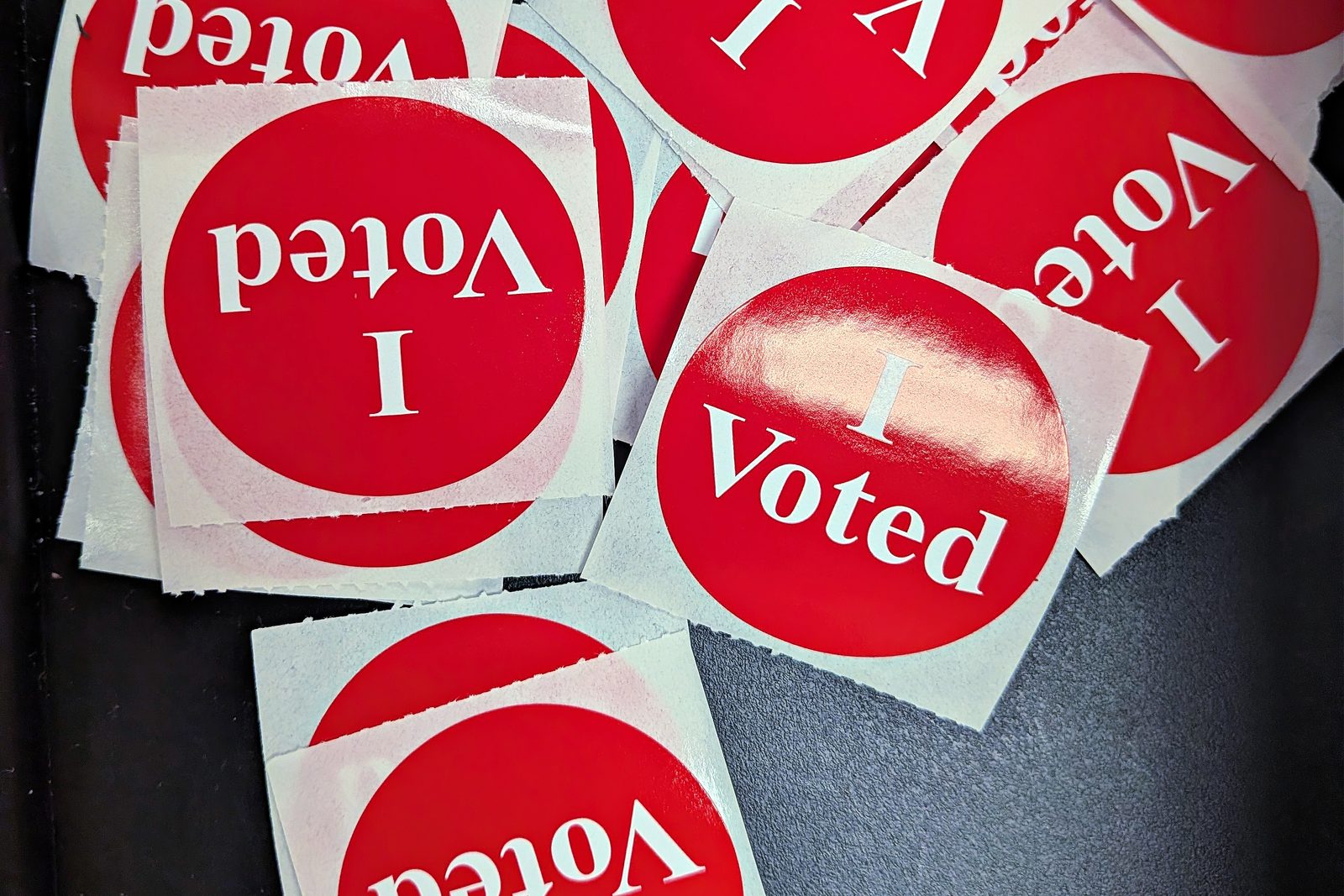 A pile of red and white I Voted stickers on a dark table at a polling place